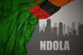 Abstract silhouette of the city with text Ndola near waving colorful national flag of zambia on a gray background