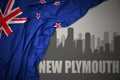 Abstract silhouette of the city with text New Plymouth near waving national flag of new zealand on a gray background