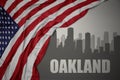 Abstract silhouette of the city with text Oakland near waving colorful national flag of united states of america on a gray