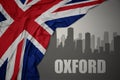 Abstract silhouette of the city with text Oxford near waving national flag of great britain on a gray background