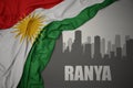 Abstract silhouette of the city with text Ranya near waving national flag of kurdistan on a gray background.3D illustration