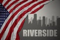 Abstract silhouette of the city with text Riverside near waving colorful national flag of united states of america on a gray