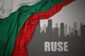 Abstract silhouette of the city with text Ruse near waving national flag of bulgaria on a gray background