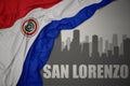 Abstract silhouette of the city with text San Lorenzo near waving national flag of paraguay on a gray background