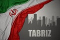 Abstract silhouette of the city with text Tabriz near waving national flag of iran on a gray background.3D illustration