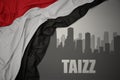 Abstract silhouette of the city with text Taizz near waving national flag of yemen on a gray background Royalty Free Stock Photo