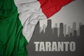 Abstract silhouette of the city with text Taranto near waving national flag of italy on a gray background