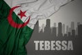 Abstract silhouette of the city with text Tebessa near waving colorful national flag of algeria on a gray background