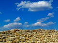 Brown stone wall detail with blue sky and fluffy cumulus clouds Royalty Free Stock Photo