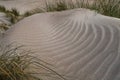 A abstract wavy pattern in a small sand caused by the wind, tufts of grass in the foreground and background Royalty Free Stock Photo