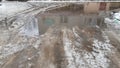 Blurry reflection of old building in dirty water of large puddle with melting snow on road. Bad weather conditions in winter. Royalty Free Stock Photo