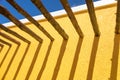 Abstract Wood Posts and Bright Yellow Wall Against Blue Sky