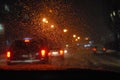 Abstraction. Blurred night urban view with cars, bright traffic lights through wet car windshield in blurred rain drops Royalty Free Stock Photo