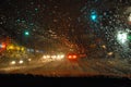 Abstraction. Blurred night urban view with cars, bright traffic lights through wet car windshield in blurred rain drops Royalty Free Stock Photo