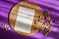 Abstraction, on purple background, wicker round stand and on it lies empty piece of paper for text, around scattered colored pasta