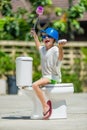 Absurd picture: cute boy dancing on the toilet, which is installed in the middle of the street. Pan on his head Royalty Free Stock Photo