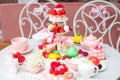 Abundant assortment of sugar dessert treats with present box and teapot on white table with chairs in cafe or restaurant
