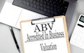 ABV -ACCREDITED IN BUSINESS VALUATION word on clipboard on laptop with calculator and pen