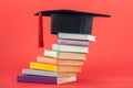 Academic cap with tassel and bright books on red surface.