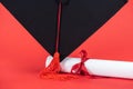 Academic cap with tassel and diploma with ribbon on red surface.