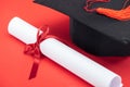 Academic cap with tassel and diploma with ribbon on red surface.