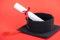 Academic cap with tassel and diploma with ribbon on red surface.