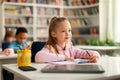 Academic concept. Smart caucasian school girl sitting at desk in classroom, listening teacher and writing in notebook Royalty Free Stock Photo