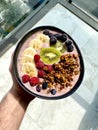 Acai Smoothie Bowl with Baked Granola, Blueberries, Raspberry, Banana and Kiwi in Hand