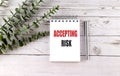 Accepting risk phrase on spiral notebook with silver pen and green leaves on wooden table Royalty Free Stock Photo