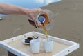 Accessories for alternative brewing coffee on a tray on the sandy beach. Barista spills coffee on cups