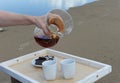 Accessories for alternative brewing coffee on a tray on the sandy beach. Barista spills coffee on cups