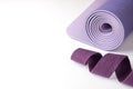 Accessories for yoga, pilates or fitness. Purple yoga mat and purple belt on a white background with copyspace