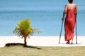 Accident tourist girl are walking up by crutches on the white sand beach while travel