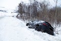 Accident on a winter snowy track with a black car skidding and falling into a ditch due to ice. Safety and poor driving on the