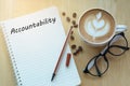 Accountability concept on notebook with glasses, pencil and coffee cup on wooden table. Business concept.