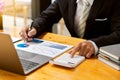 An accountant using a calculator and computer with a pen in hand is making money and analyzing graph papers on the table about exp