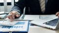 An accountant using a calculator and computer with a pen in hand is making money and analyzing graph papers on the table about exp