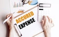 Accrued expense phrase on clipboard with charts, calculator and hands using pen on white background Royalty Free Stock Photo