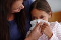 Achoo. a mother helping her sick daughter to blow her nose.