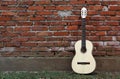 Acoustic guitar leaning on grunge red brick wall. Grass on pavement Royalty Free Stock Photo