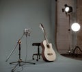 Acoustic guitar and microphone in recording studio with spotlight on background.