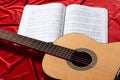 Acoustic guitar and music notes on red fabric, close view of objects Royalty Free Stock Photo