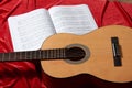 Acoustic guitar and music notes on red fabric, close view of objects Royalty Free Stock Photo