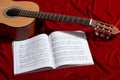 Acoustic guitar and music notes on red velvet fabric, close view of objects Royalty Free Stock Photo