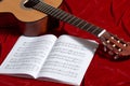 Acoustic guitar and music notes on red velvet fabric, close view of objects Royalty Free Stock Photo