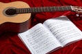 Acoustic guitar and music notes on red velvet fabric, close view of objects