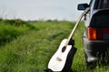 Acoustic guitar next to a black car in nature