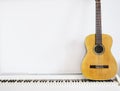 Acoustic guitar on piano keyboard in front of white wall