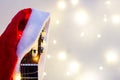 Acoustic Guitar with red Santa hat and light garland. Christmas music song concept with copyspace Royalty Free Stock Photo