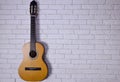 An acoustic guitar stands upright against a light brick wall on the left side. Plenty of space on the right for caption or text Royalty Free Stock Photo